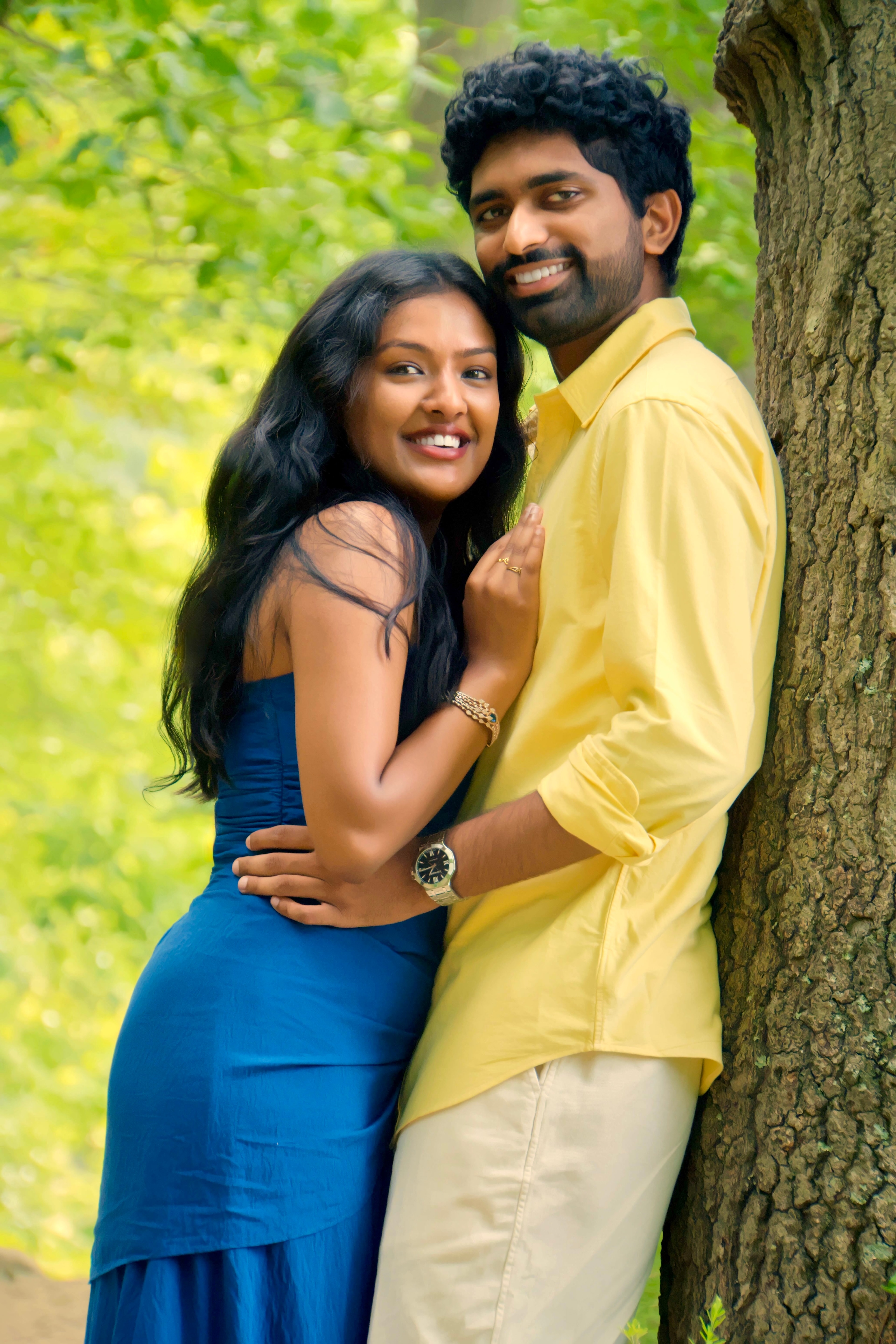 Aarti and Anish smiling together beside a tree